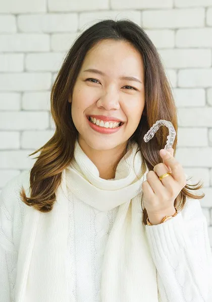 Smiling woman in white turtleneck against brick wall background for orthodontics practice.