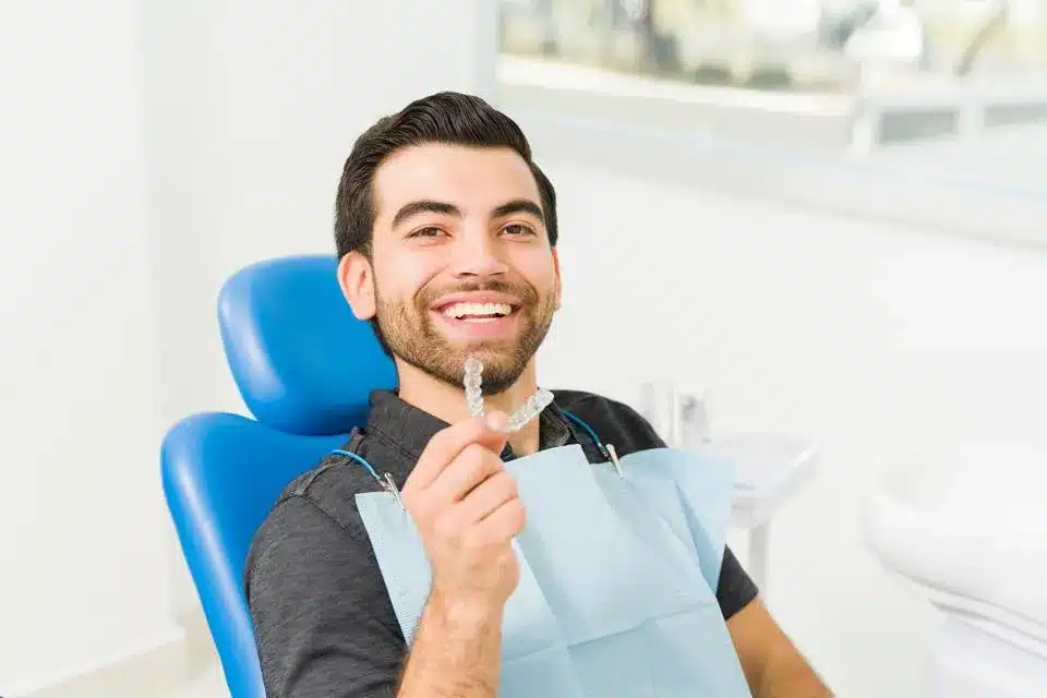 Happy male patient in dental chair touching face, smiling at orthodontic clinic