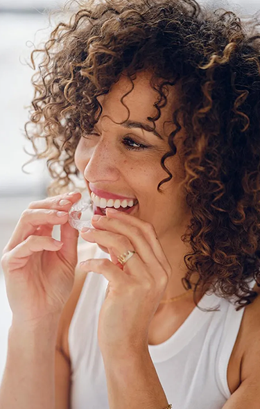 Woman with curly hair smiling while flossing teeth, bright dental hygiene setting.