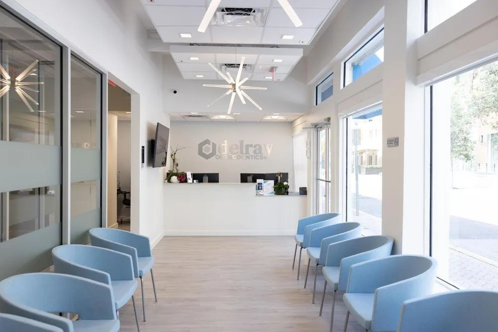 Modern dental waiting room with blue seating, white reception desk, and bright natural lighting.