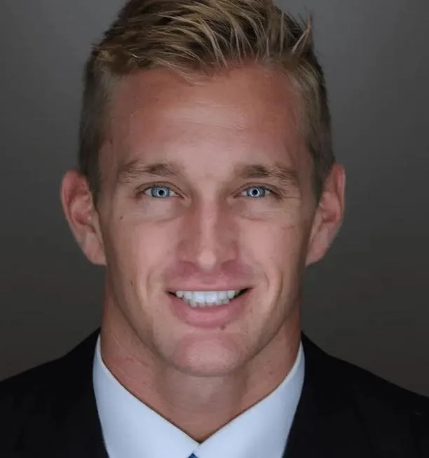 Professional headshot of smiling man in business suit and tie against gray background.
